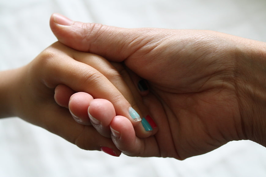 Close-up of adult and child holding hands with painted nails