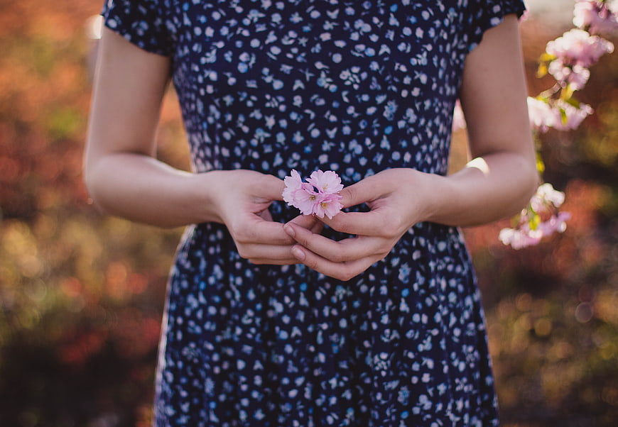 Woman holding pink cherry blossoms in blue floral dress