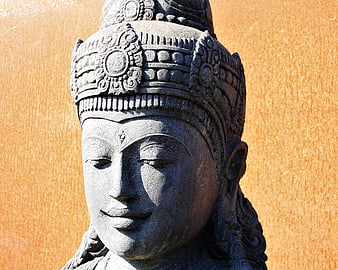 Close-up of serene stone Buddha head sculpture against orange wall