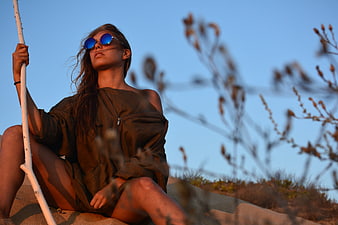 Woman in sunglasses sitting on sand dune at sunset