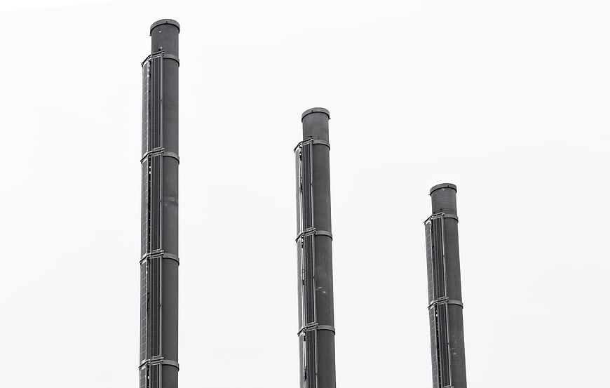 Three tall industrial smokestacks against white sky