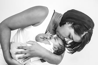 Black and white portrait of a mother kissing her sleeping newborn baby