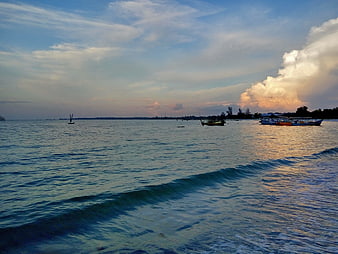 Ocean waves and boats at sunset with dramatic clouds