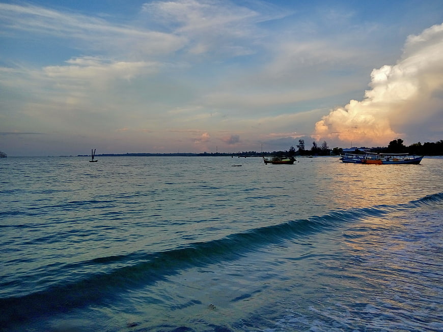 Ocean waves and boats at sunset with dramatic clouds