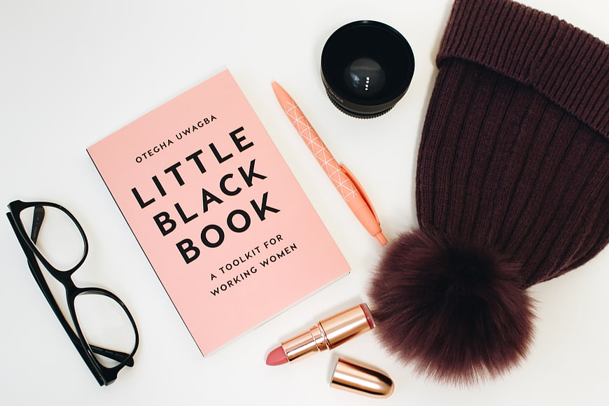 Flat lay of Little Black Book, glasses, lipstick, and beanie