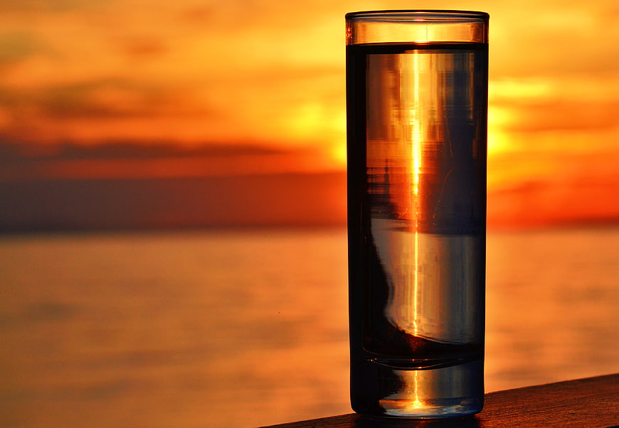 Glass of Water with Sunset Reflection by the Sea