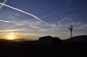 Silhouette of windmill and barn at sunrise with contrails