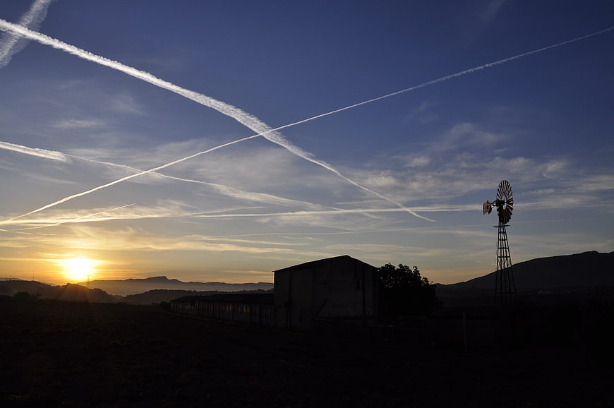 Silhouette of windmill and barn at sunrise with contrails