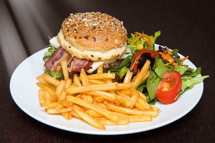 Delicious Bacon Cheeseburger with Fries and Salad on White Plate