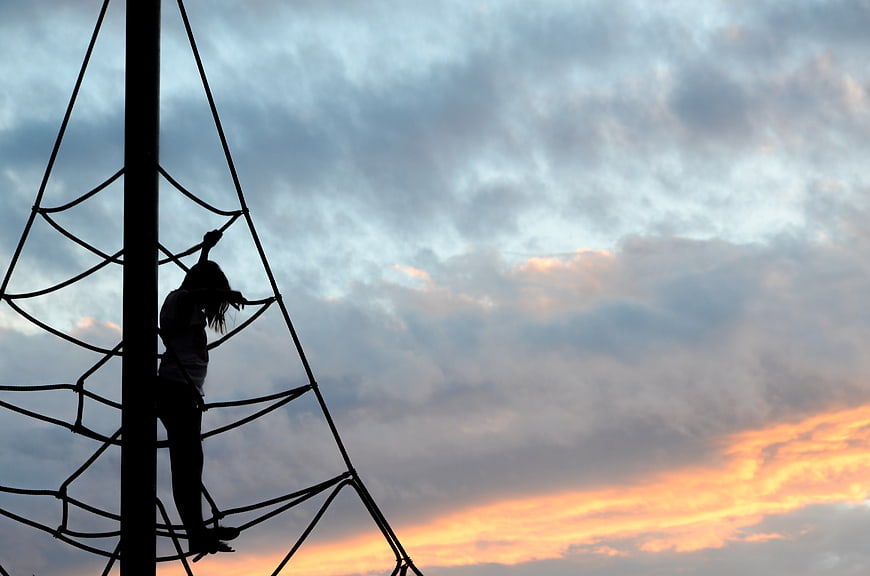 Silhouette of Girl Climbing Rope Net at Sunset