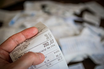 Hand holding a printed receipt with financial figures and blurred background