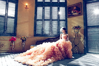 Elegant woman in voluminous peach ruffled gown sitting on vintage balcony