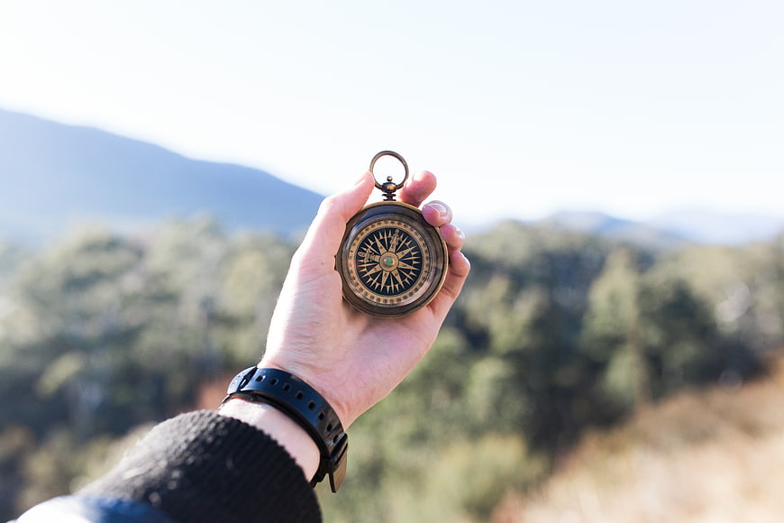 Hand holding vintage compass against blurred mountain landscape