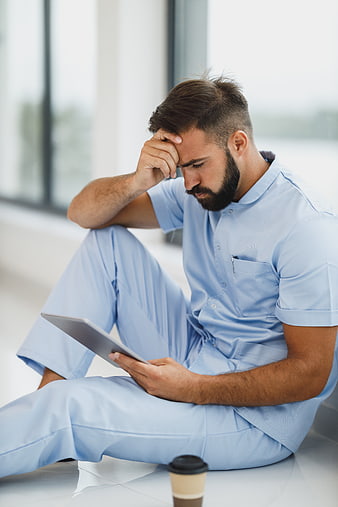 Stressed male nurse sitting on floor with tablet and coffee