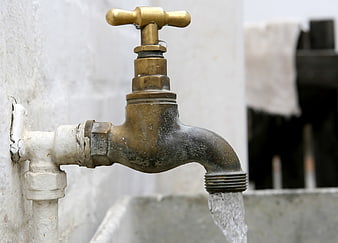 Old brass faucet with running water on white wall