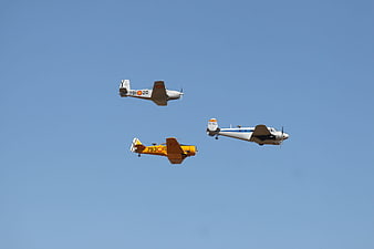 Three vintage propeller planes flying in formation against blue sky