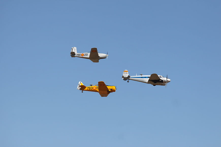 Three vintage propeller planes flying in formation against blue sky