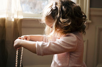 Little girl playing with pearl necklace by window