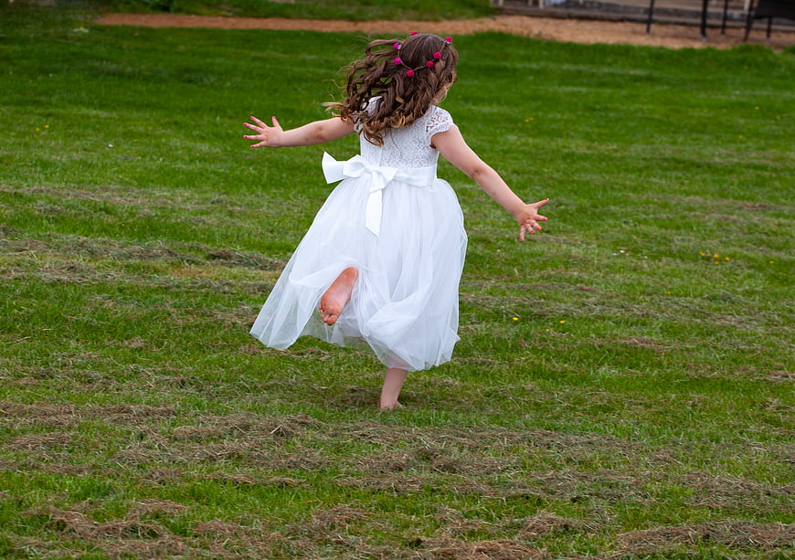 Little girl in white dress running barefoot on grass
