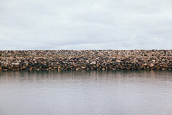 Rocky breakwater wall against calm water and overcast sky