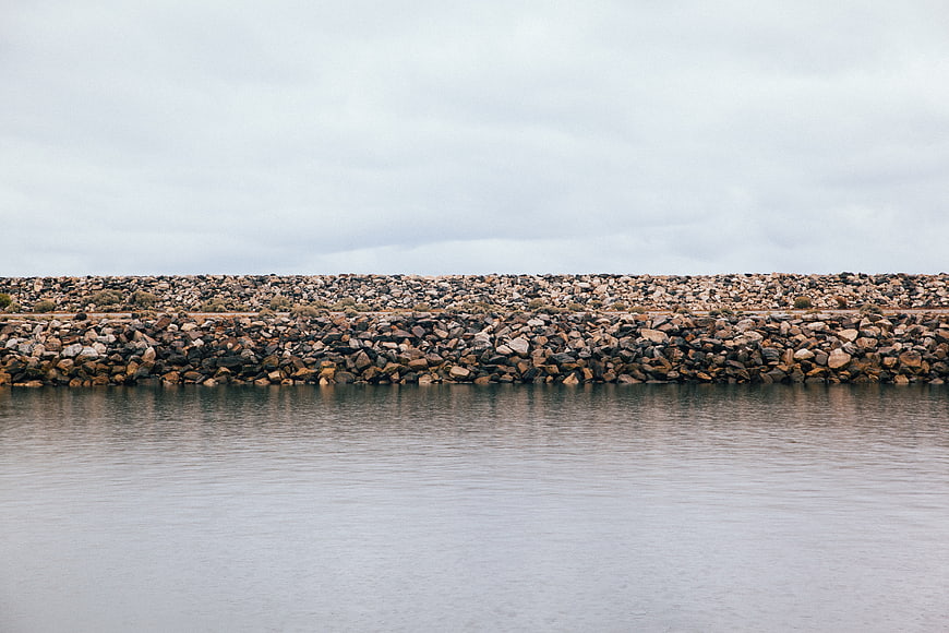 Rocky breakwater wall against calm water and overcast sky