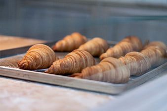 Freshly baked croissants on a metal tray in bakery display
