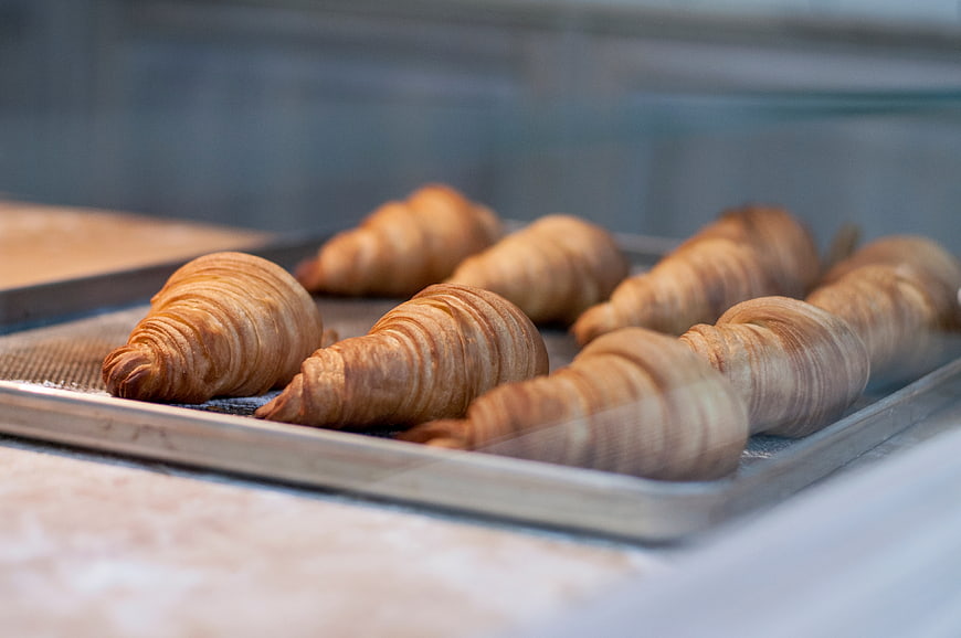 Freshly baked croissants on a metal tray in bakery display