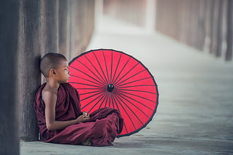 Young Buddhist Monk Meditating with Red Umbrella