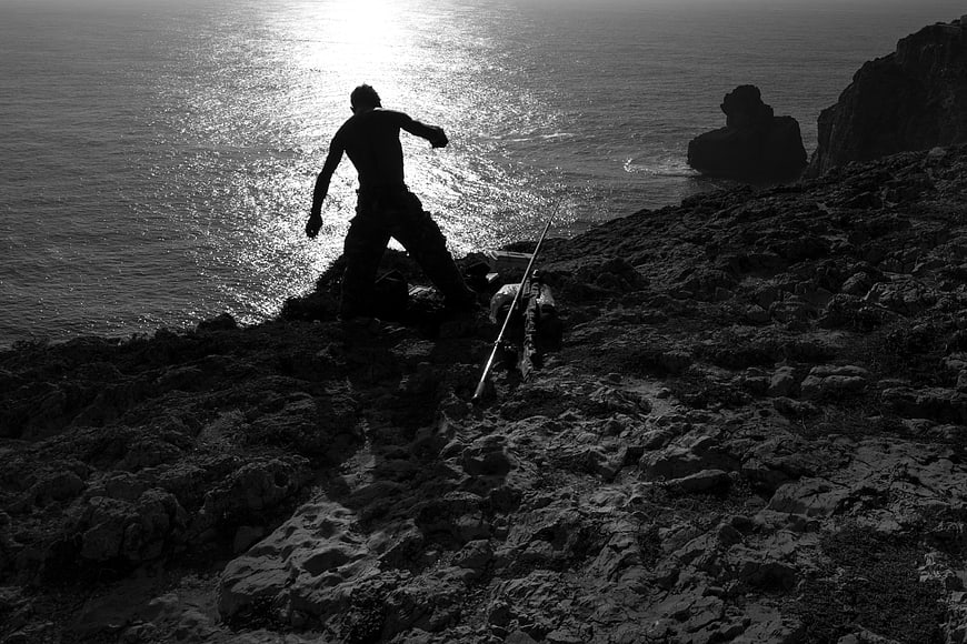 Silhouette of fisherman casting rod on rocky shore