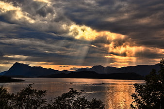 Dramatic Sunset Over Norwegian Fjord With Sunbeams And Silhouetted Mountains
