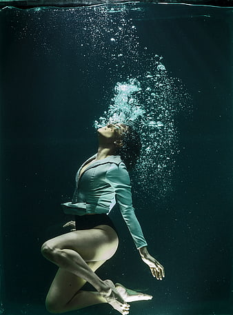Underwater fashion portrait of a woman in a teal jacket with rising bubbles