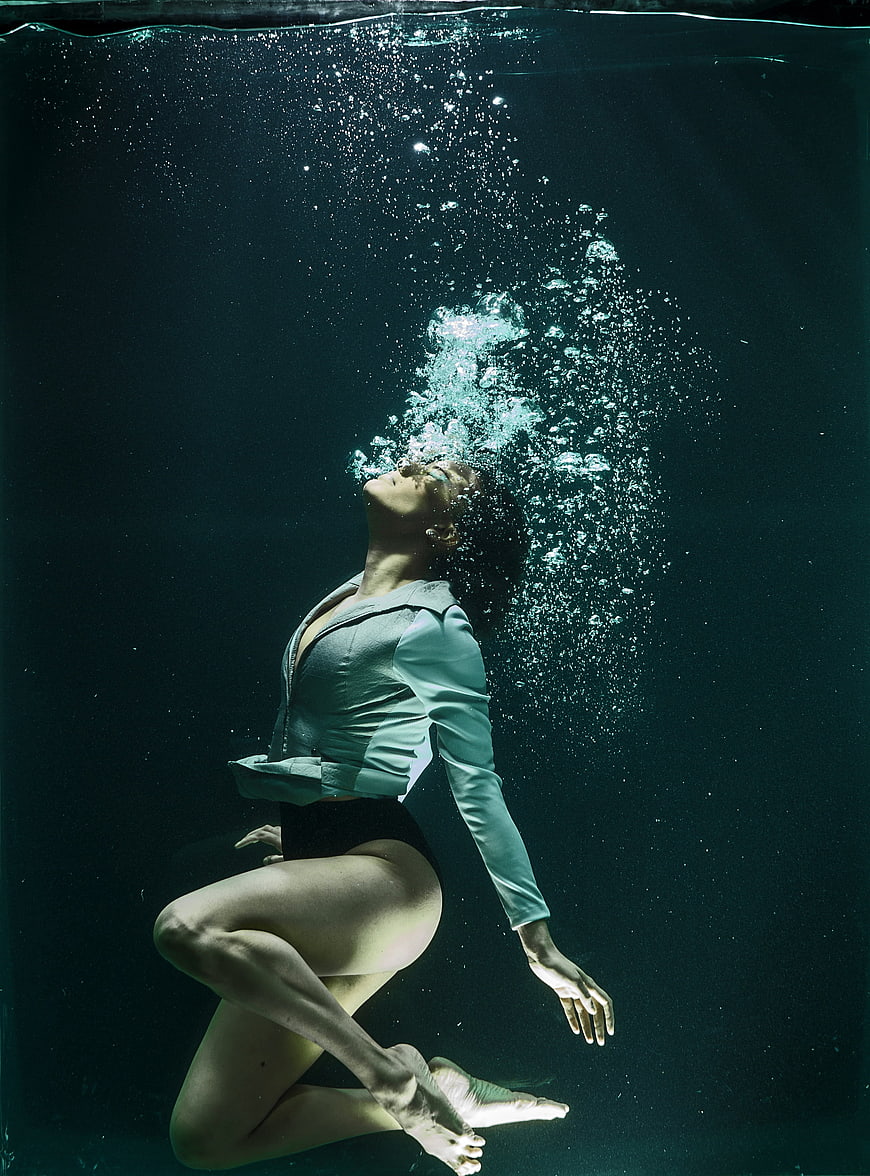 Underwater fashion portrait of a woman in a teal jacket with rising bubbles