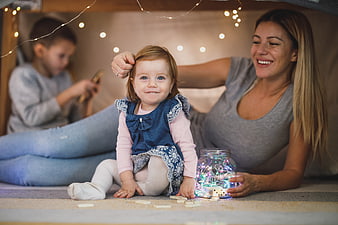 Happy mother and toddler playing with fairy lights indoors