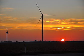 Silhouette of wind turbines against a vibrant orange sunset sky