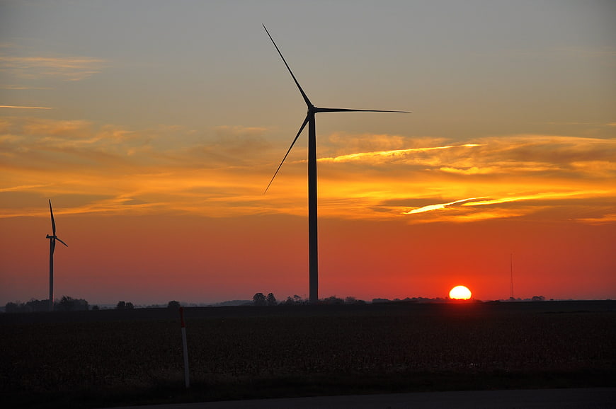 Silhouette of wind turbines against a vibrant orange sunset sky