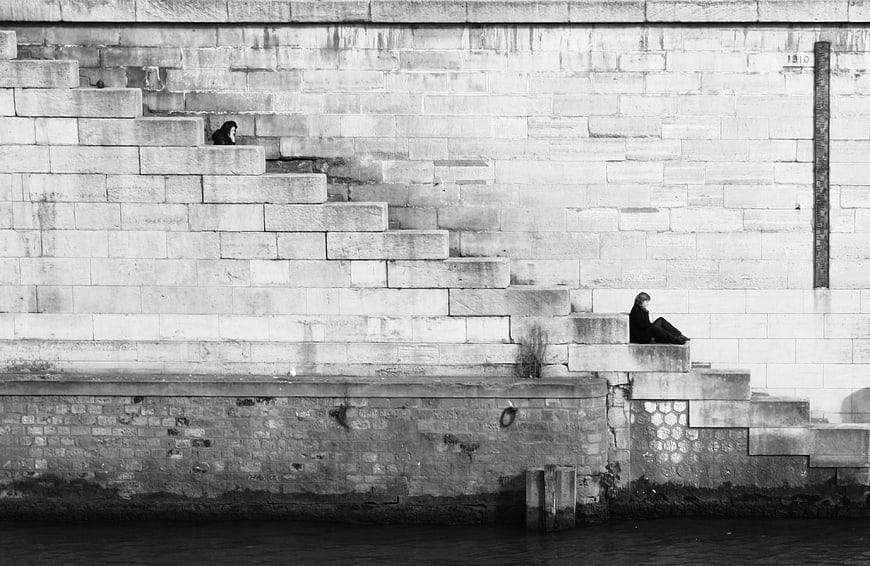 Black and white photo of woman sitting on stone stairs by river