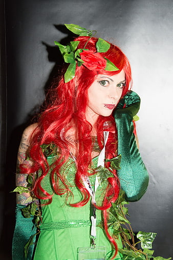 Woman in green floral cosplay costume with red hair and flower crown
