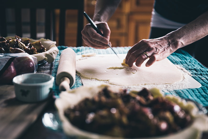 Hands Cutting Pie Crust with Knife on Kitchen Table