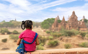 Young girl in pink shirt sitting on ledge overlooking ancient temples in Myanmar