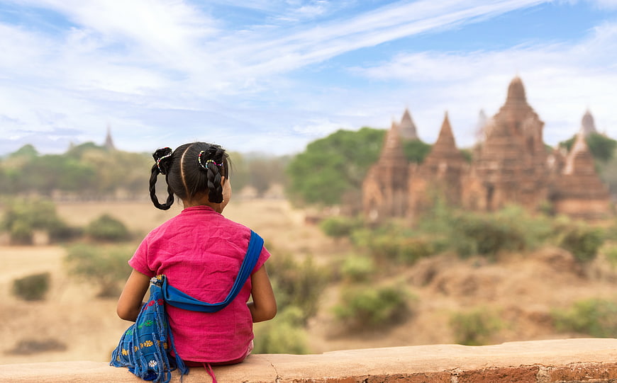 Young girl in pink shirt sitting on ledge overlooking ancient temples in Myanmar