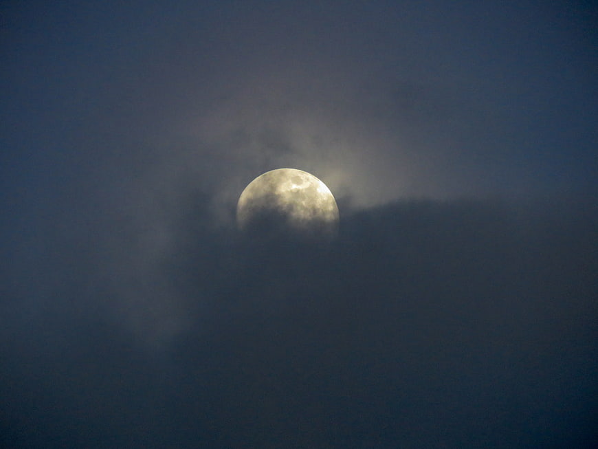 Full moon glowing through dark clouds at night