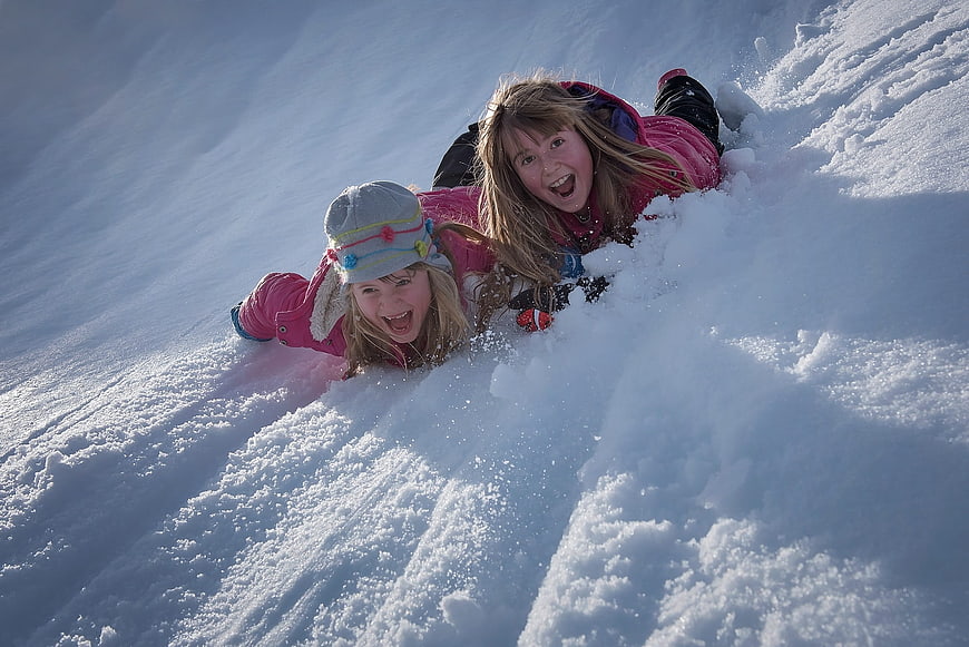 Two girls sledding down a snowy hill with joyful expressions