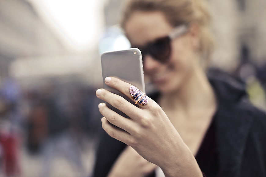 Woman with sunglasses using smartphone with colorful ring
