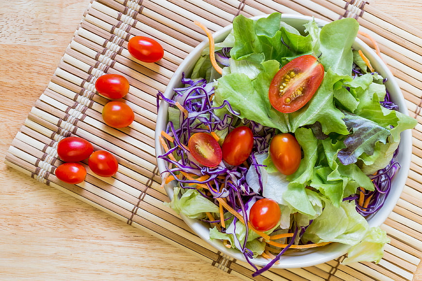 Fresh vegetable salad bowl with tomatoes and cabbage on bamboo mat