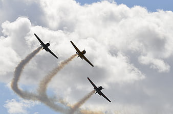 Three vintage propeller planes performing aerobatics with smoke trails