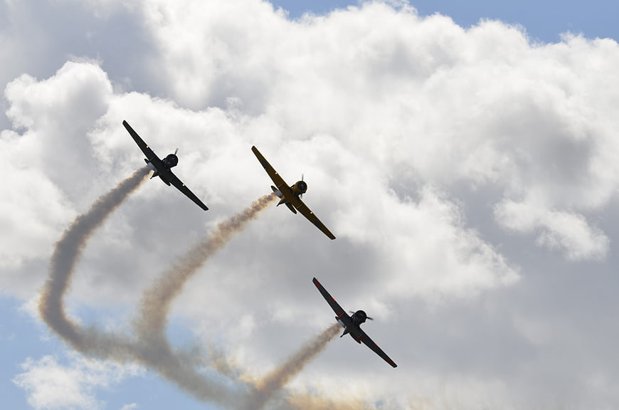 Three vintage propeller planes performing aerobatics with smoke trails