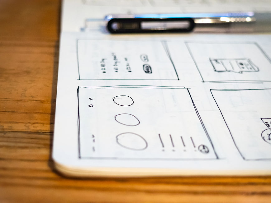Hand-drawn UI wireframes in sketchbook on wooden desk