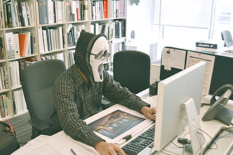 Man wearing Ghostface mask working at office desk