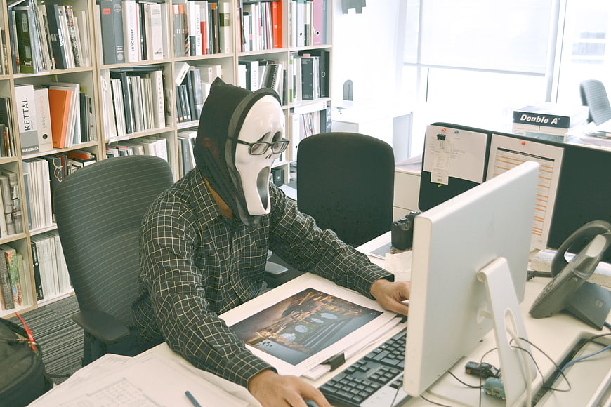 Man wearing Ghostface mask working at office desk