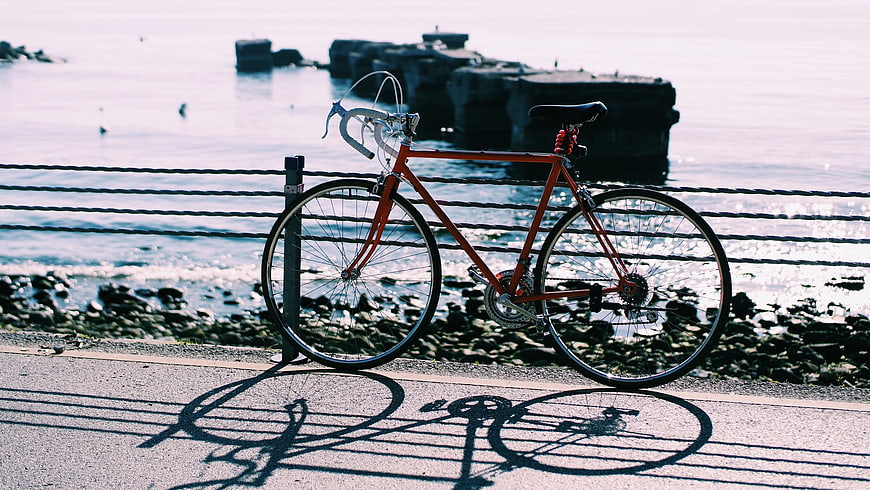 Red bicycle parked by the seaside with dramatic shadows